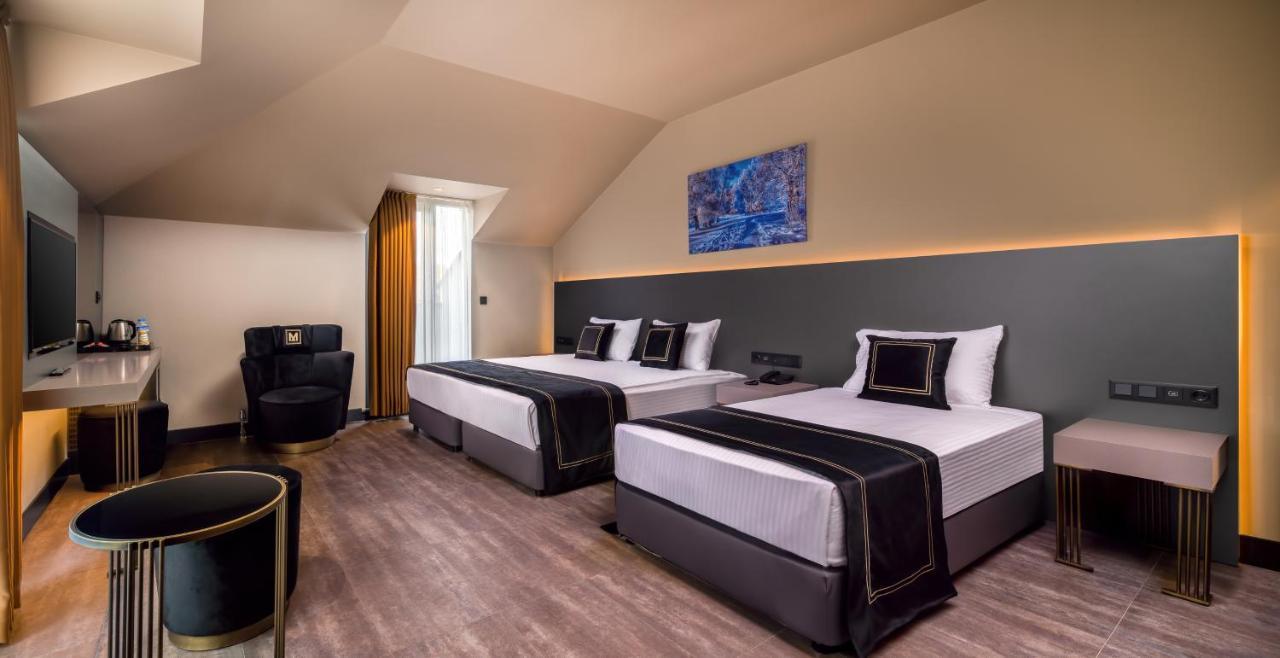 Menalo Hotel Premium Istanbul Airport Exterior foto The photo depicts a modern hotel room featuring two beds with black and white bedding. The walls are painted in neutral tones, with a contrasting dark panel behind the beds. There is a piece of blue artwork hung above the headboard. A large window is