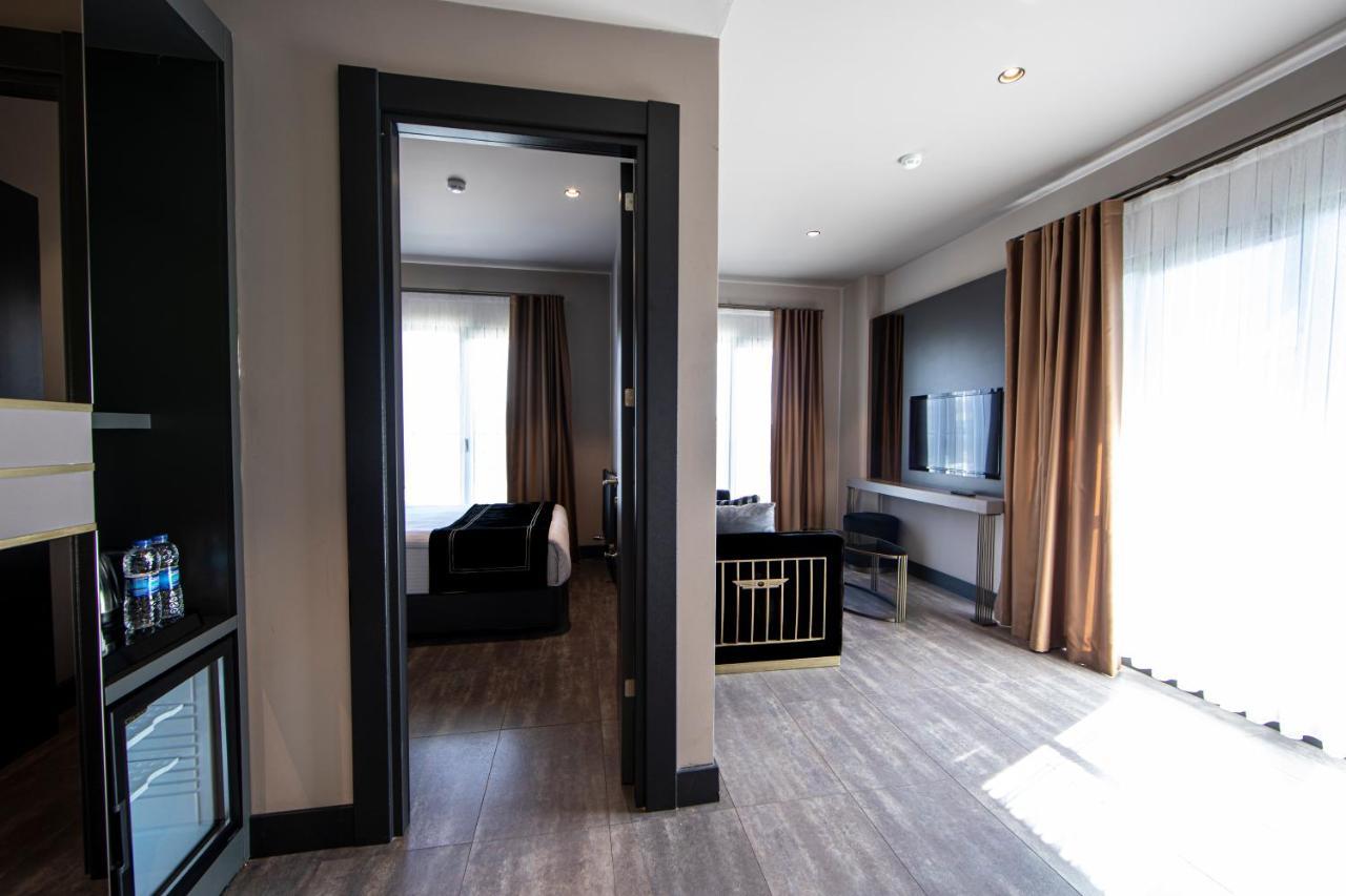 Menalo Hotel Premium Istanbul Airport Exterior foto The photo shows an interior space, likely a hotel room or a suite. It features a doorway leading to another room, with light-colored walls and wooden floors. On the left, there is a mini-fridge with drinks, and in the main area, there are large windo