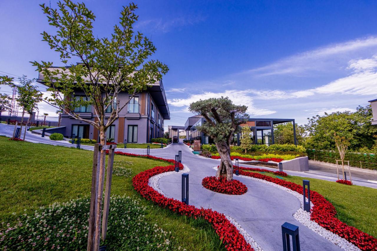 Menalo Hotel Premium Istanbul Airport Exterior foto The photo depicts a beautifully landscaped area featuring modern architecture. There are several contemporary-style buildings set against a backdrop of clear blue skies. The landscape is designed with neatly manicured grass and vibrant flower beds, p