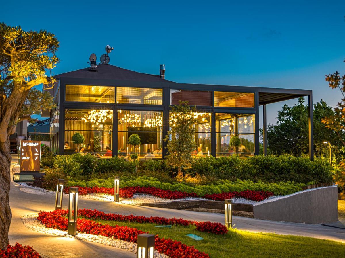 Menalo Hotel Premium Istanbul Airport Exterior foto The photo shows a modern restaurant or café building set against a twilight backdrop. The structure features large glass windows and an elegant design, allowing for visibility of the interior and the lighting within. Surrounding the building, there i
