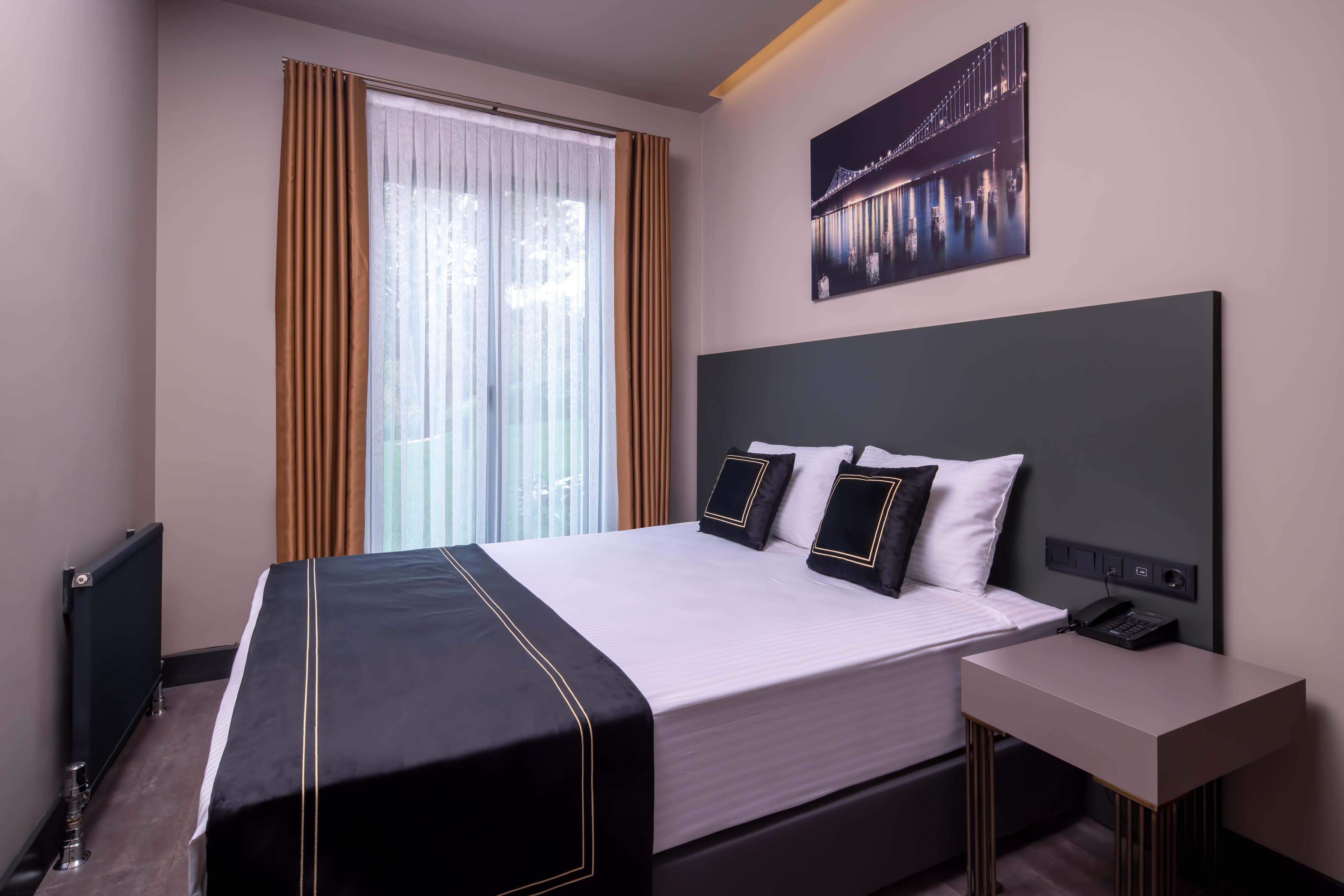 Menalo Hotel Premium Istanbul Airport Exterior foto The photo shows a modern hotel room featuring a double bed with a sleek black and white bedding set. Two decorative pillows are placed on the bed. There are large windows with sheer curtains that allow natural light to enter the room, and the walls a